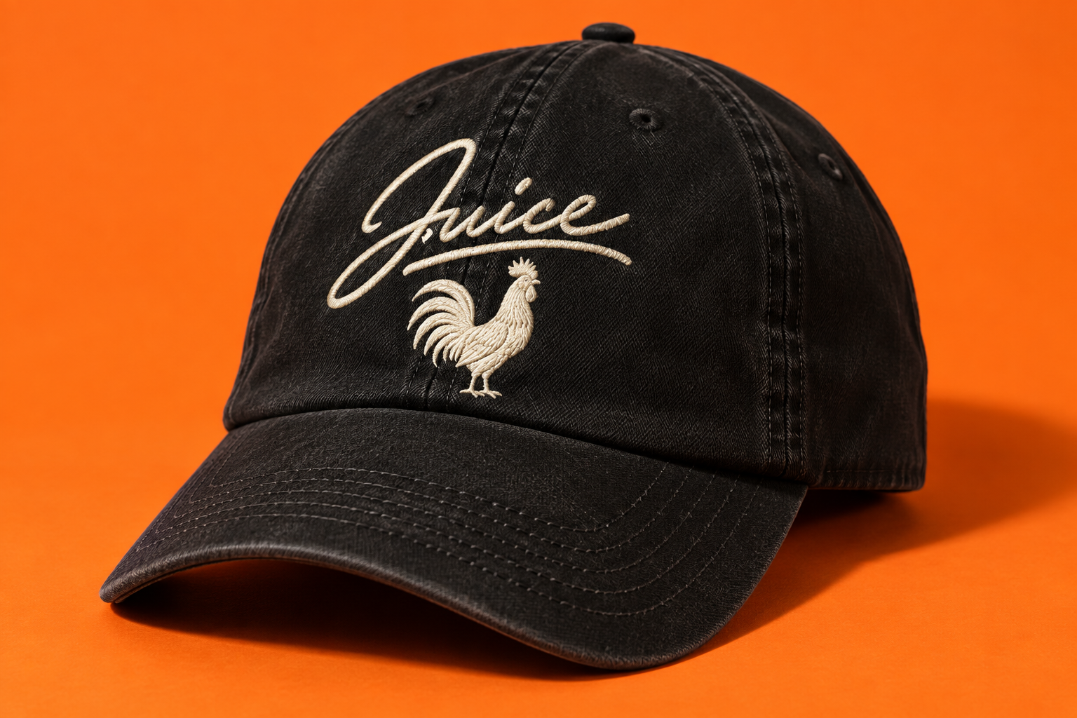 Black cap with a cream Juice signature and embroidered rooster beneath it